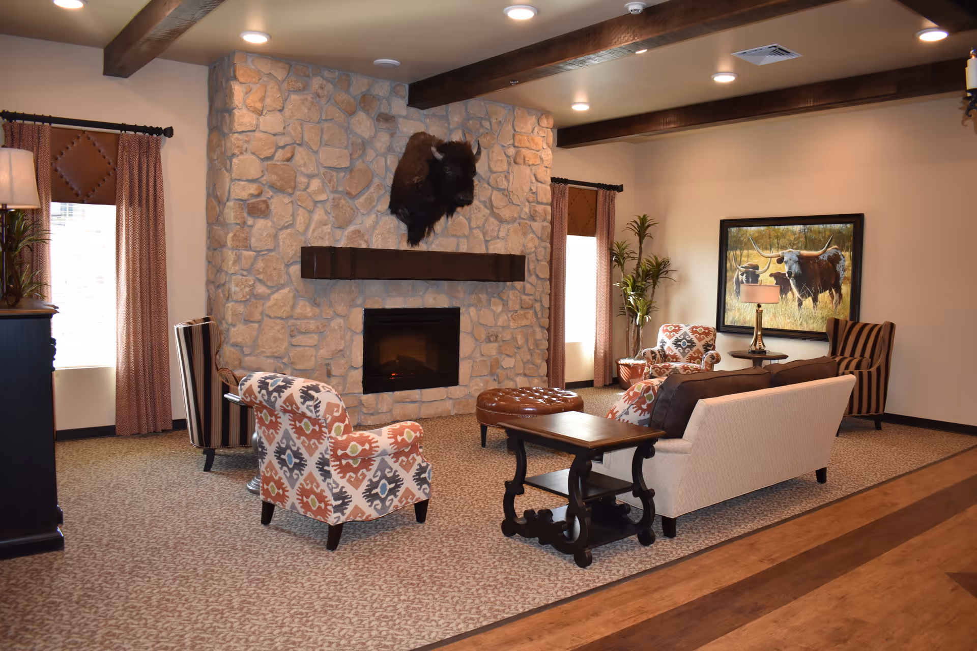Cozy living room in a senior facility with stone fireplace, sofas, chairs, and artwork.