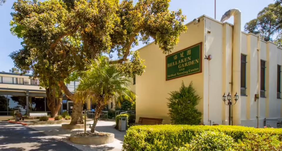 Exterior view of Bellaken Garden facility with sign, trees, and a bench.