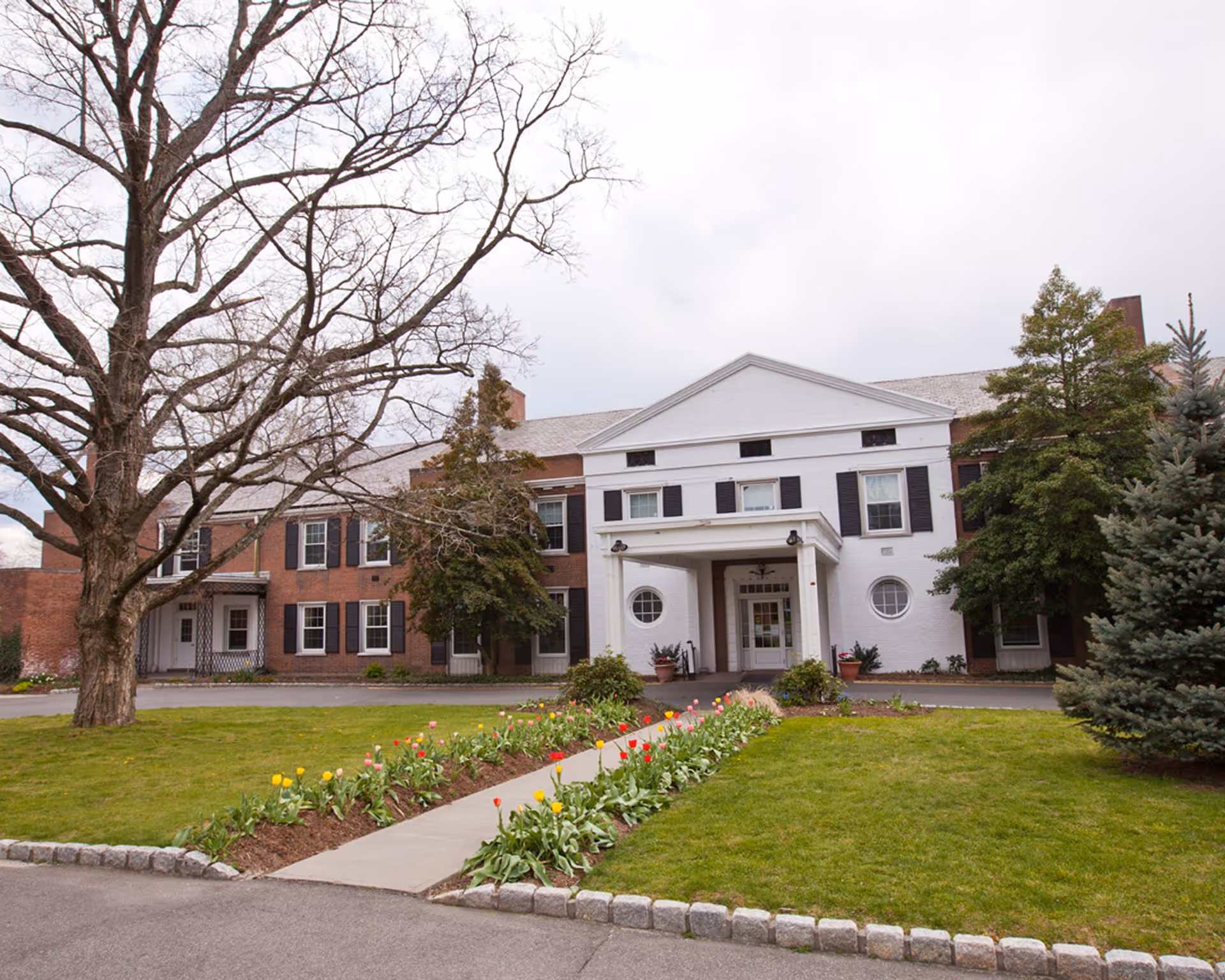 Front exterior of a two-story brick-white senior living facility with a blooming garden path.