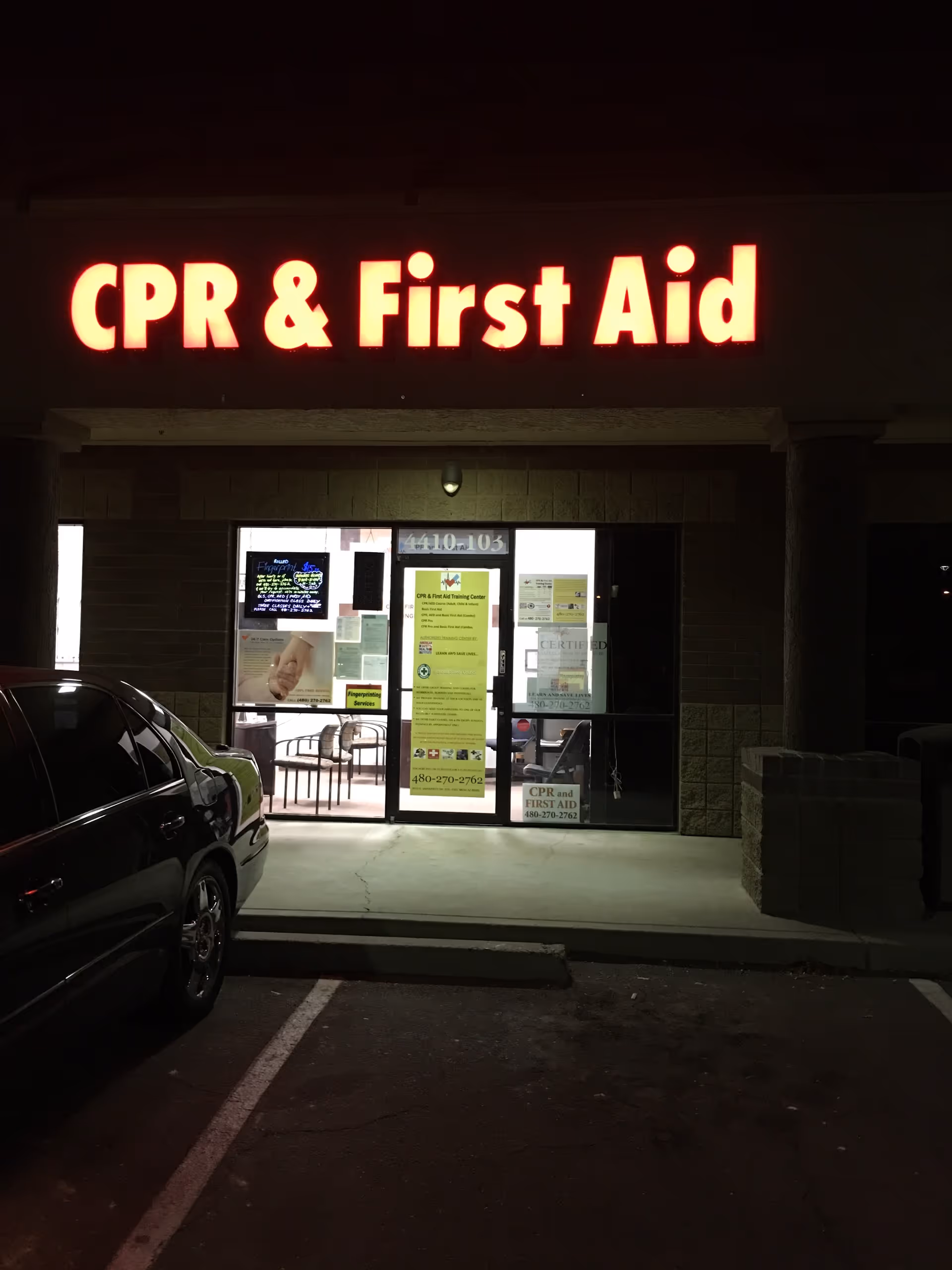 Nighttime storefront with bright red CPR and First Aid sign above glass entrance