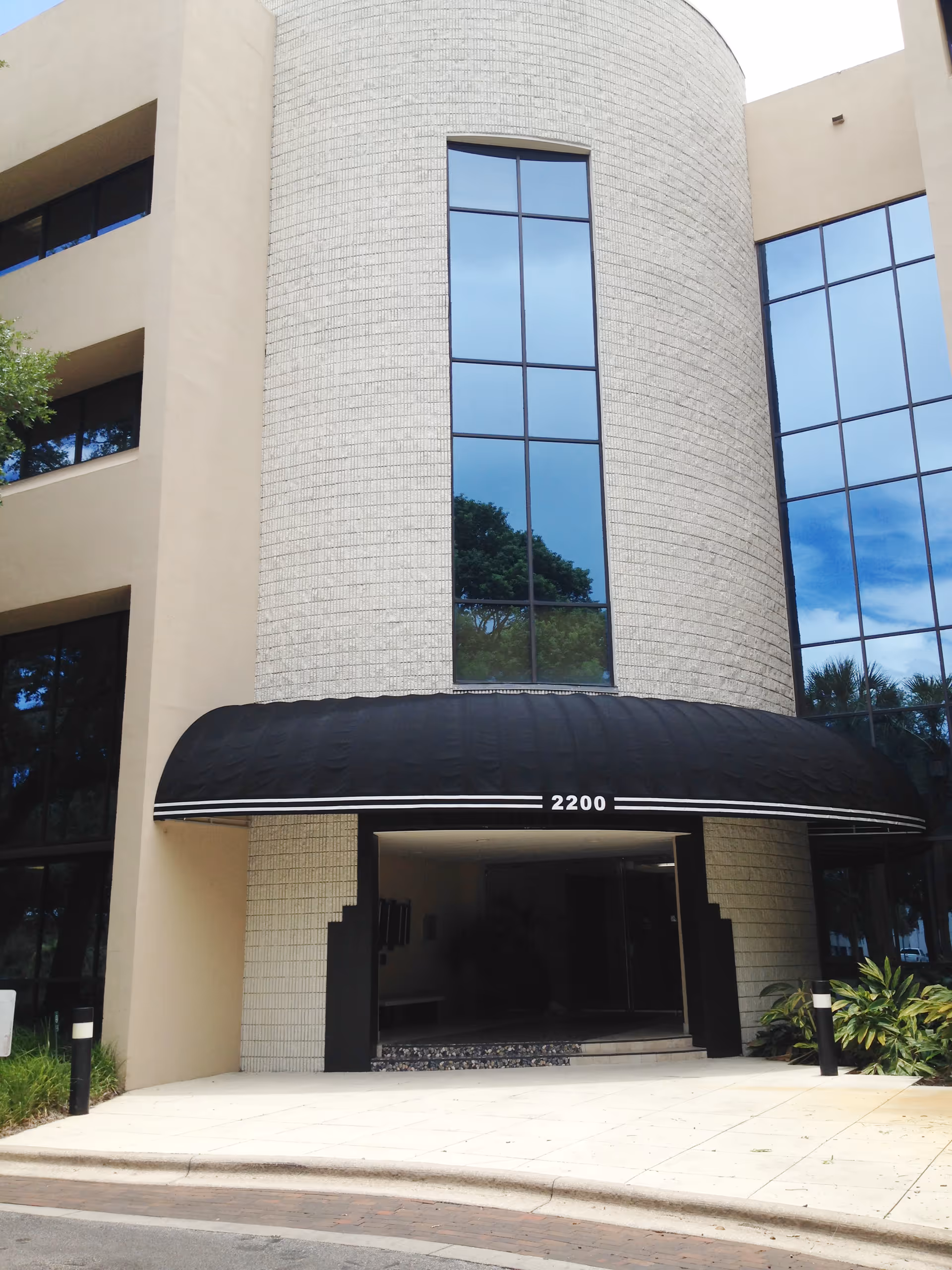 Modern senior living building front with curved tower, large glass windows, and black awning.