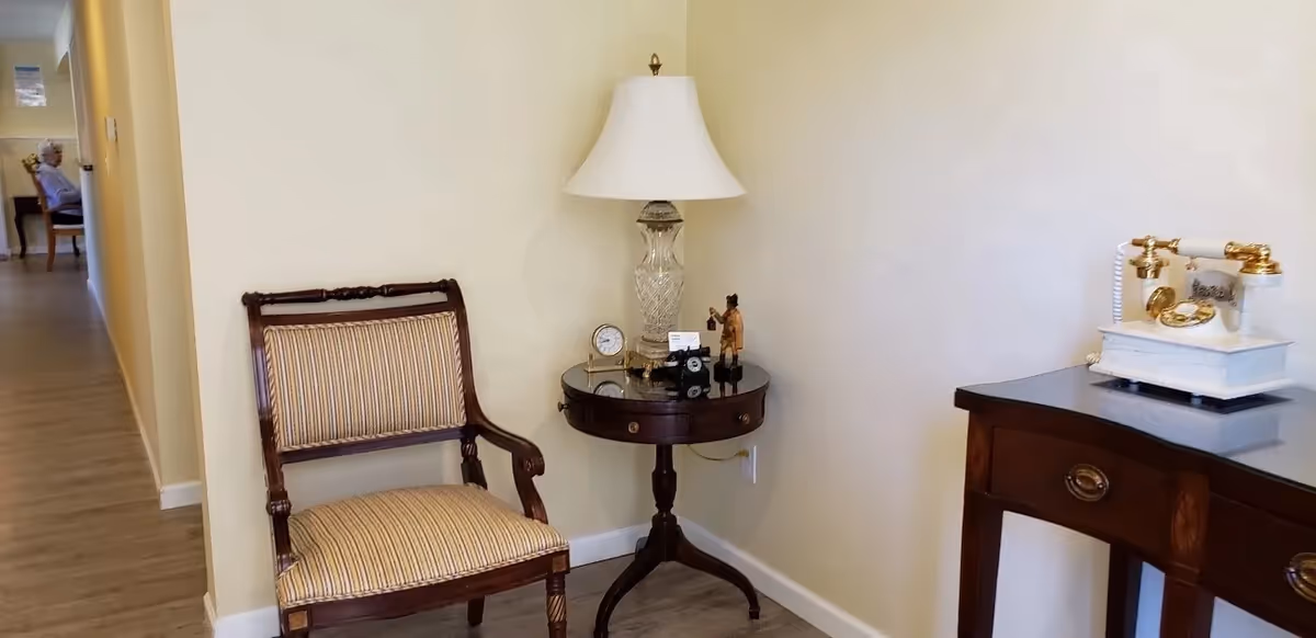 A small seating area with a striped chair, round table, lamp, and vintage telephone.