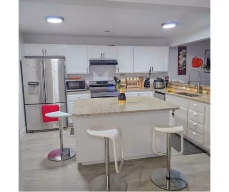 Bright, modern kitchen with island, white cabinets, stainless appliances, and a red bar stool.