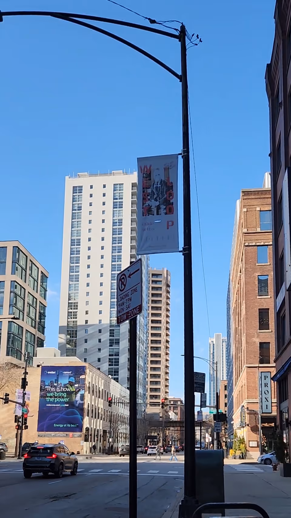 Urban street view with tall buildings, traffic, banners, and blue sky.