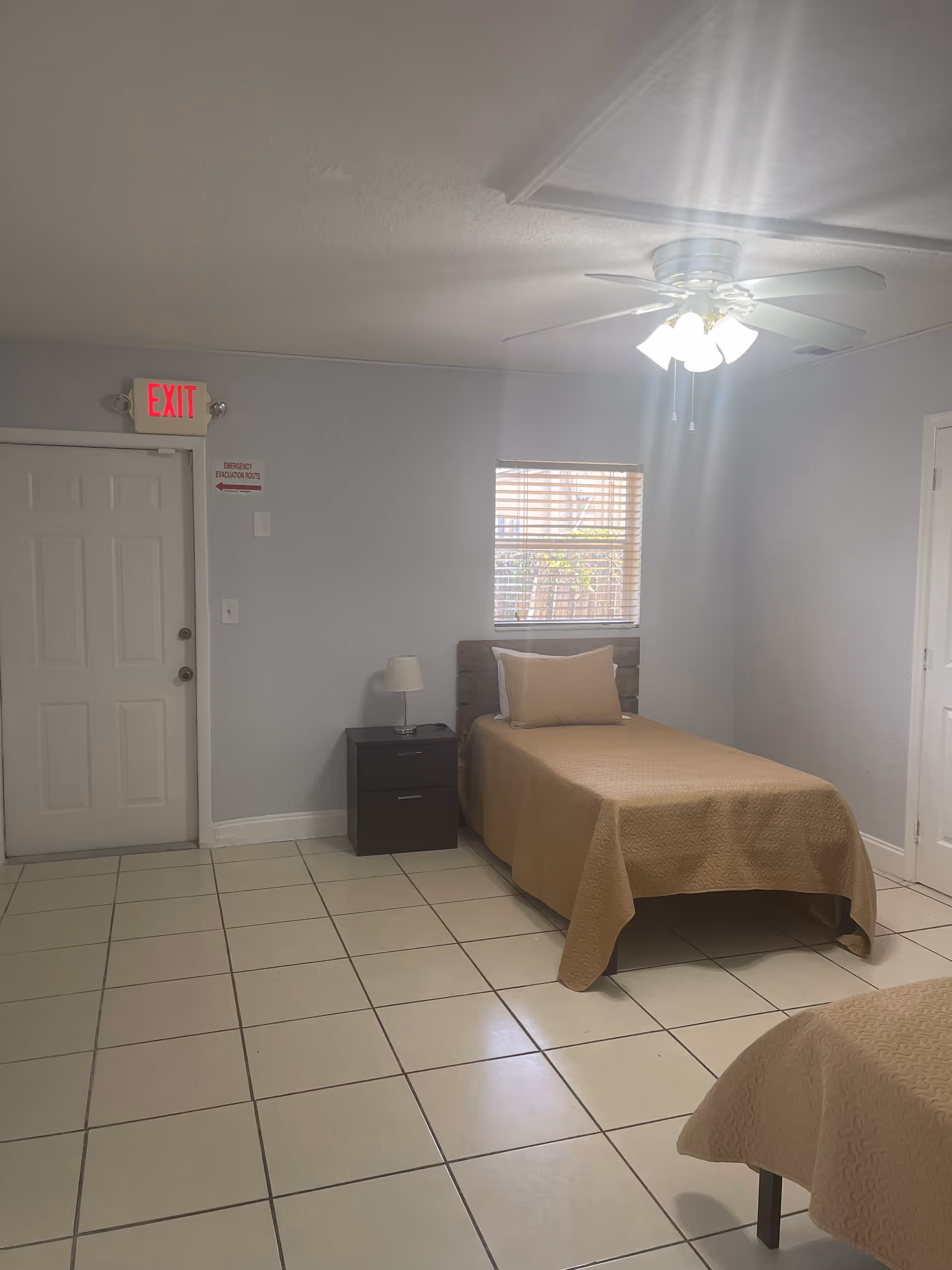 Bedroom with single bed, nightstand, lamp, window, ceiling fan, and tiled floor.