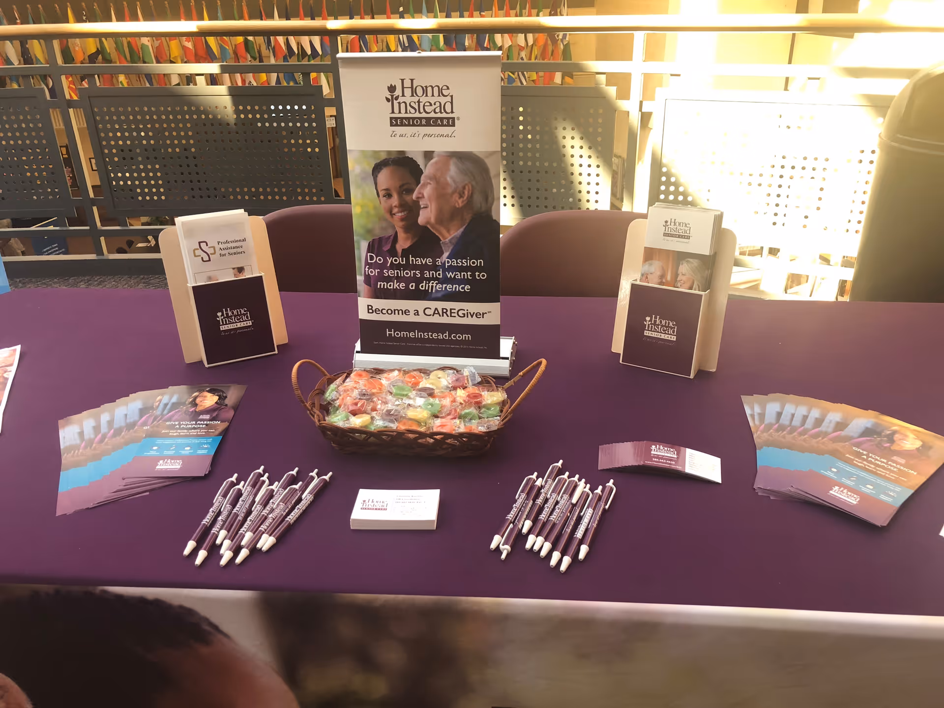Promotional table with brochures, pens, and a candy basket at indoor senior care event.