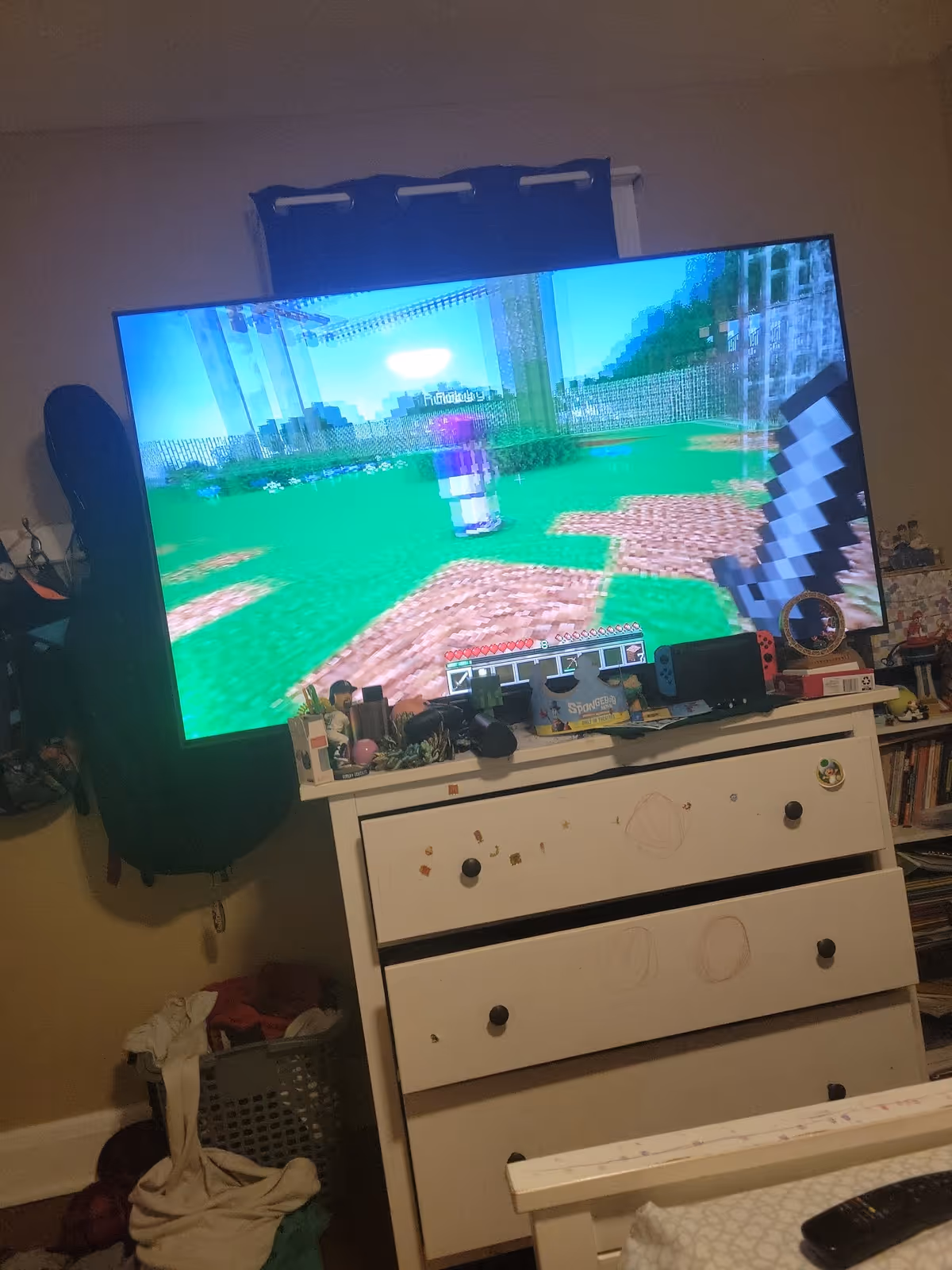 A bedroom with a large TV showing Minecraft on a white dresser.