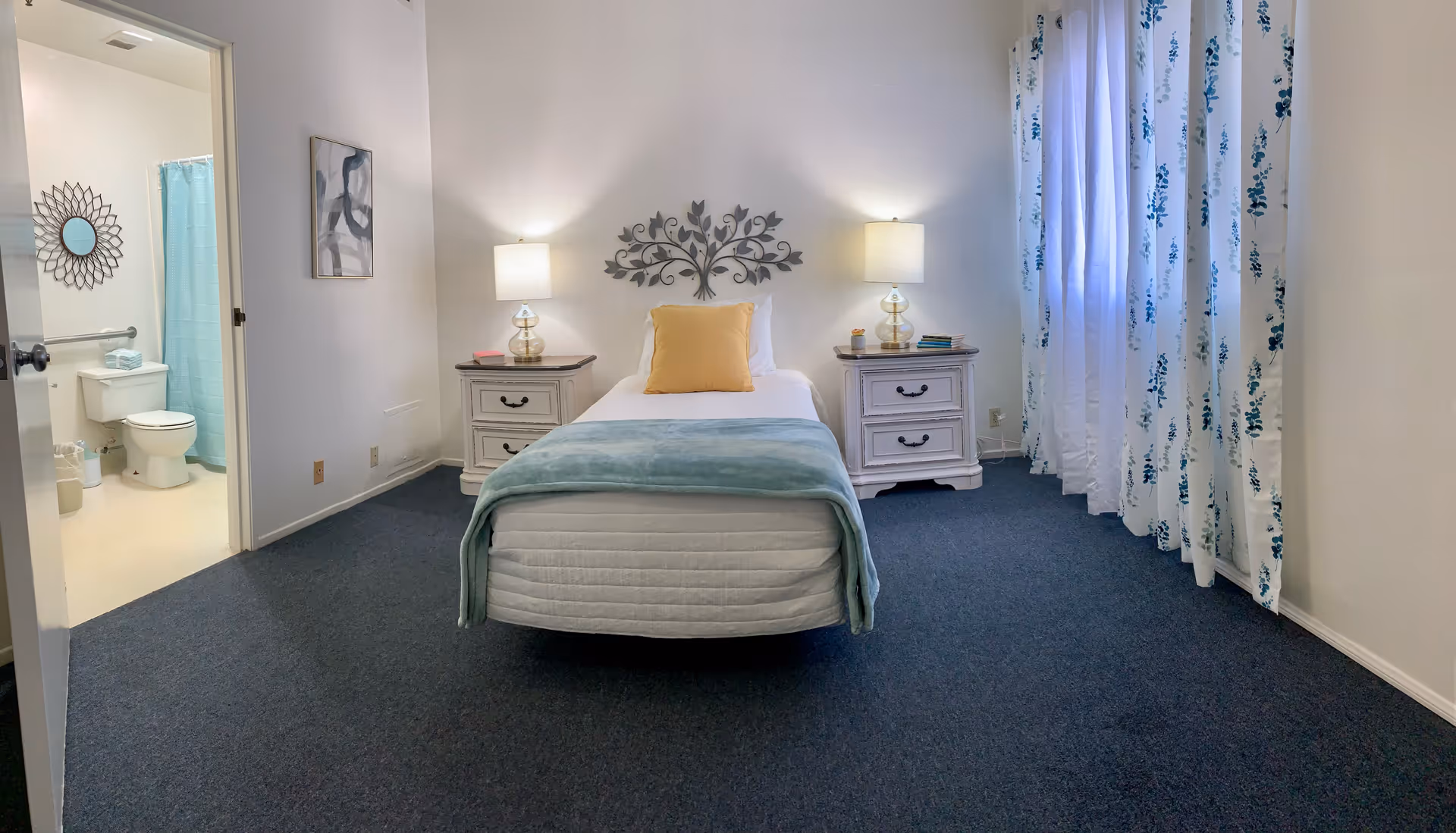 A clean bedroom with a central bed, two nightstands, lamps, and blue curtains.