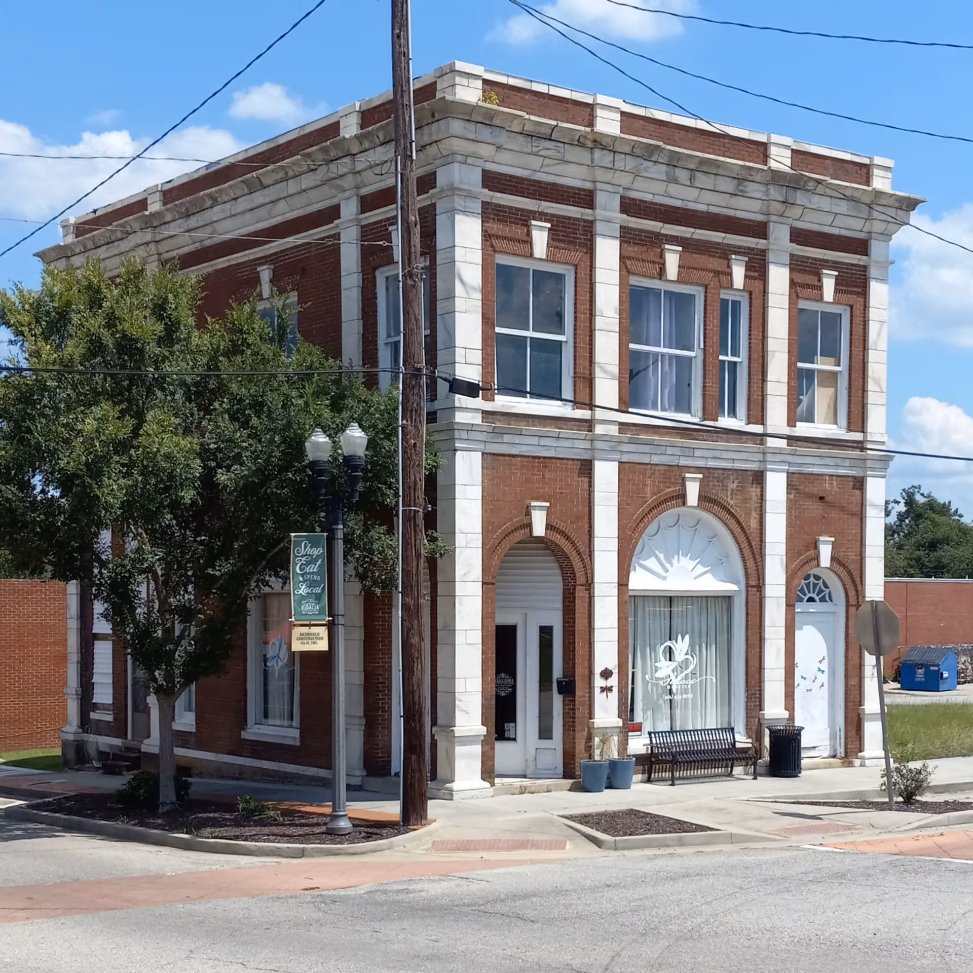 Two-story brick building with arched windows, storefronts, and a bench on the sidewalk.