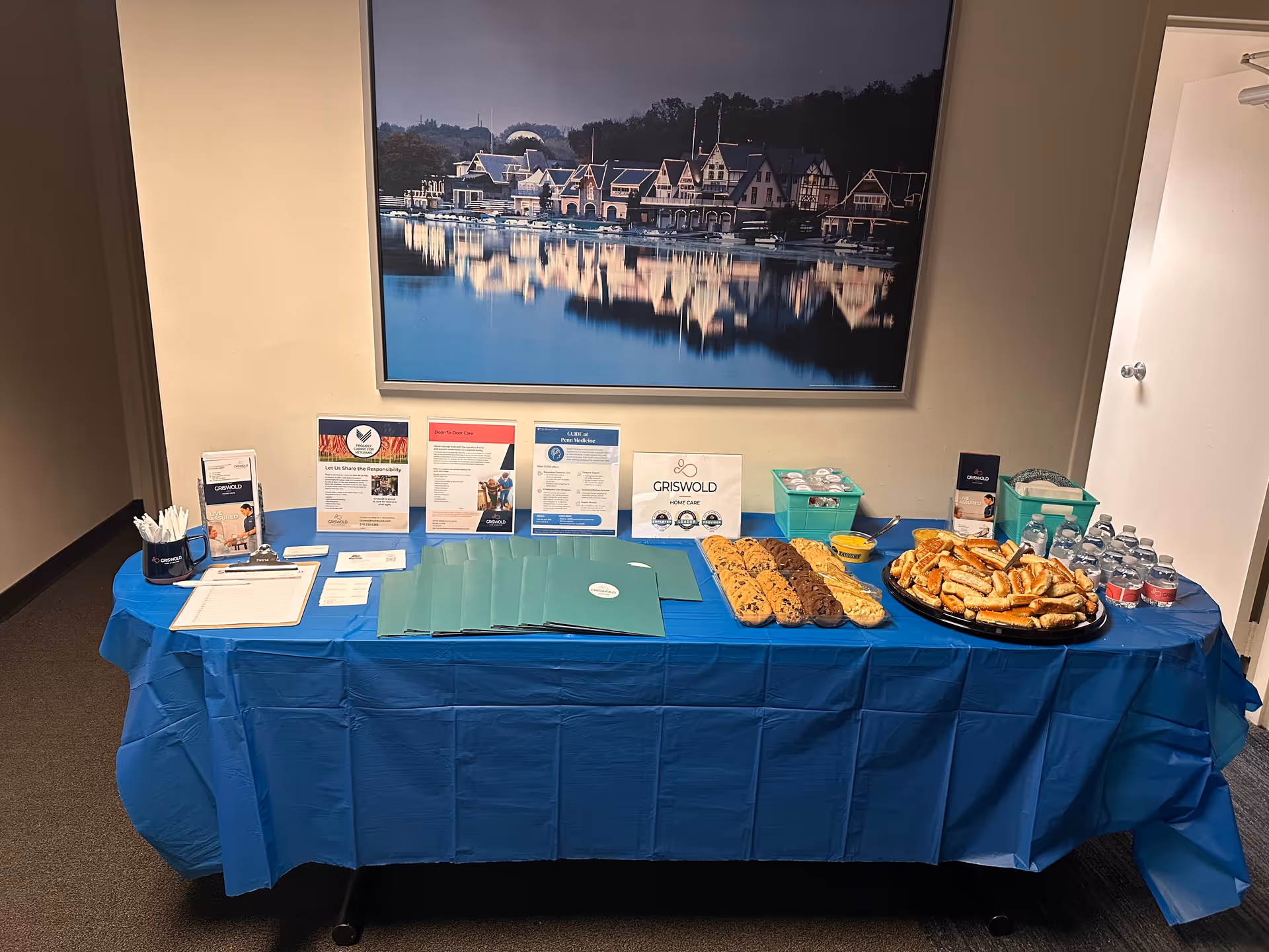 Table with blue tablecloth displaying brochures, pastries, and water bottles in Griswold Home Care lobby.