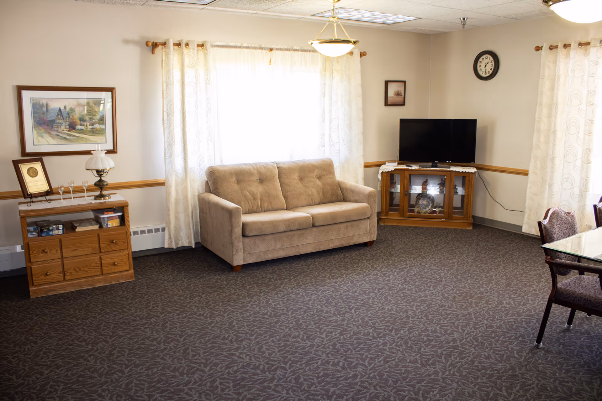 A cozy living room in a senior facility with beige sofa, TV, and wood furniture.