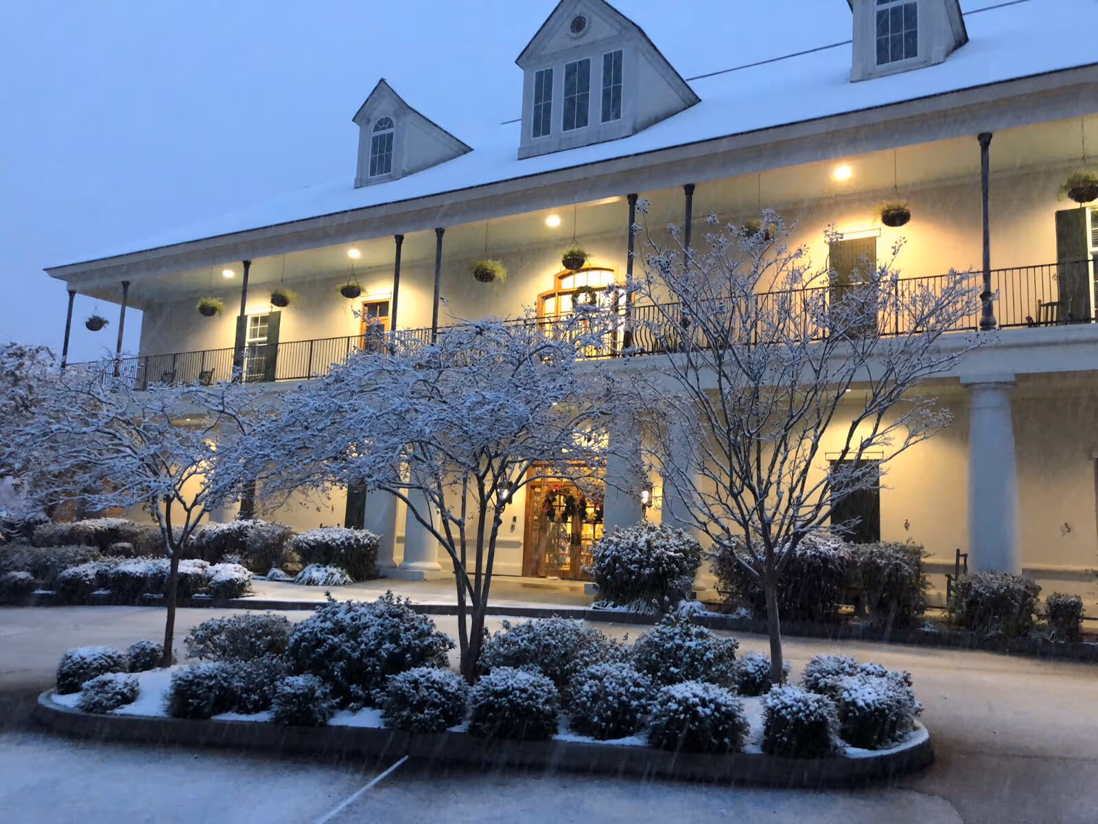 Snowy exterior of St. Joseph Hospice with lit balcony, trees, and a circular driveway.