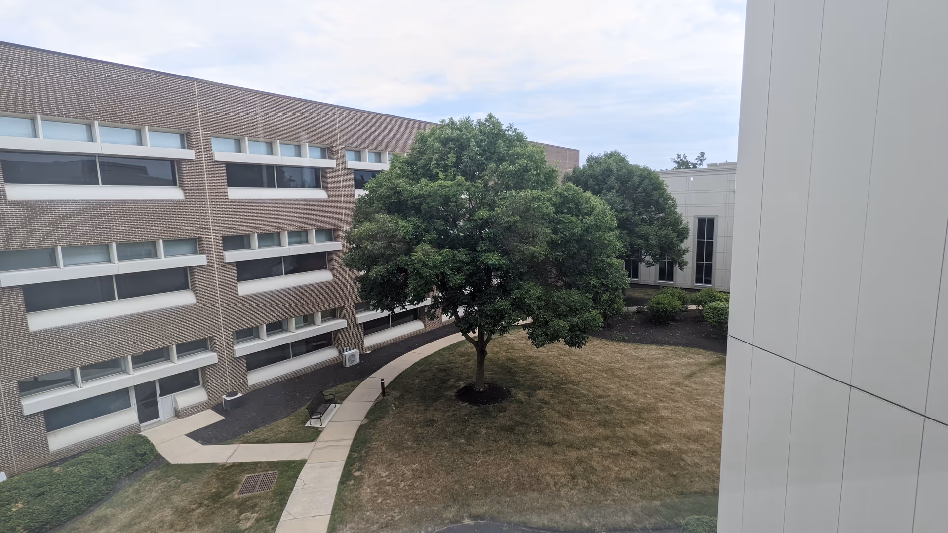 Outdoor courtyard with brick building, walkway, bench, and trees.