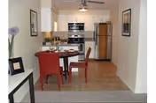 A small dining area with red chairs and a table, opening to a modern kitchen.