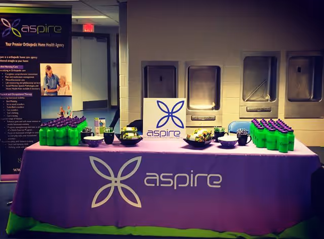 Indoor Aspire promotional table setup with purple cloth, banners, and samples.