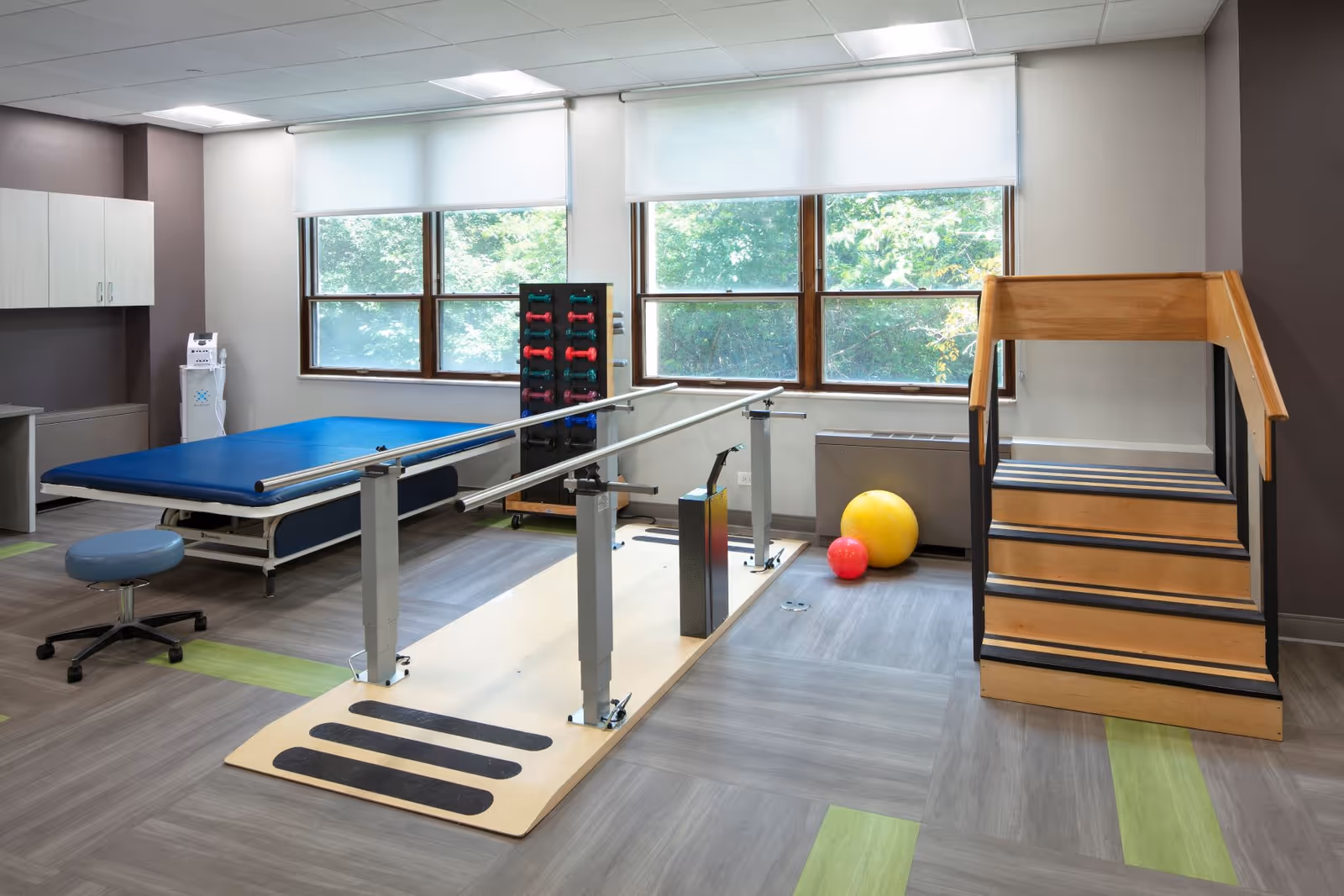 Therapy room with parallel bars, mats, stairs, and exercise equipment at Elevate Care Waukegan.