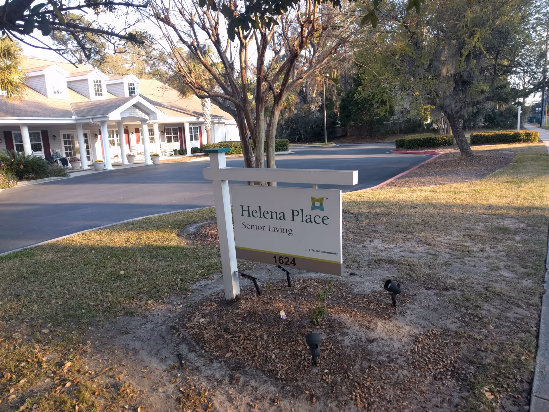 Helena Place Senior Living exterior with a sign, driveway, and a columned building facade.