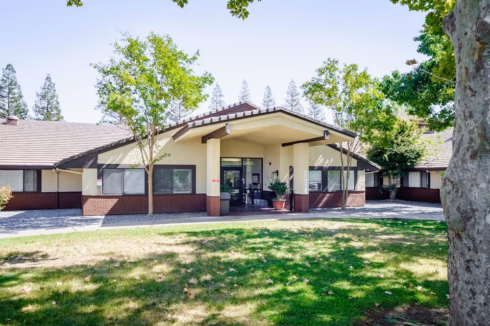 A single-story senior living center with a covered entrance, lawn, and several trees.