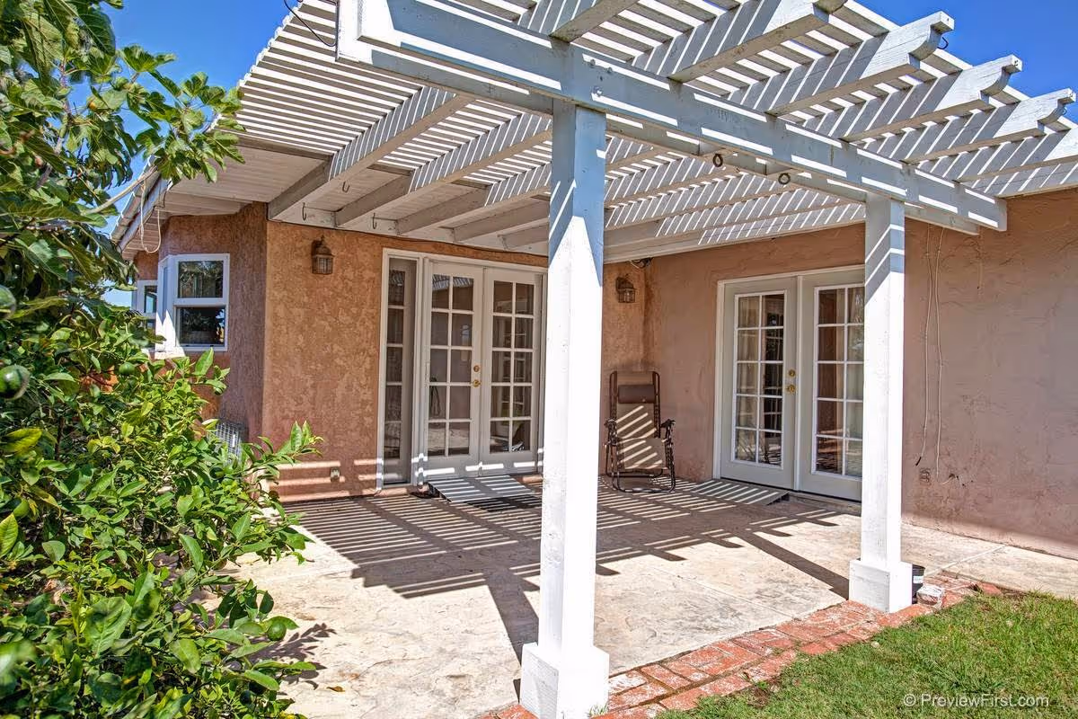 Outdoor patio with a white pergola, beige stucco walls, and French doors.