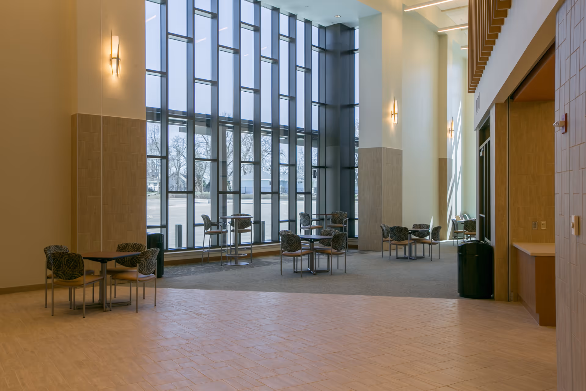 Bright hospital lobby with tall windows and scattered tables and chairs.