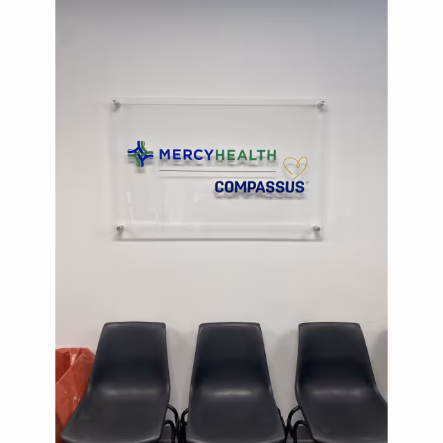 Interior lobby featuring Mercy Health Hospice by Compassus sign and three black chairs.