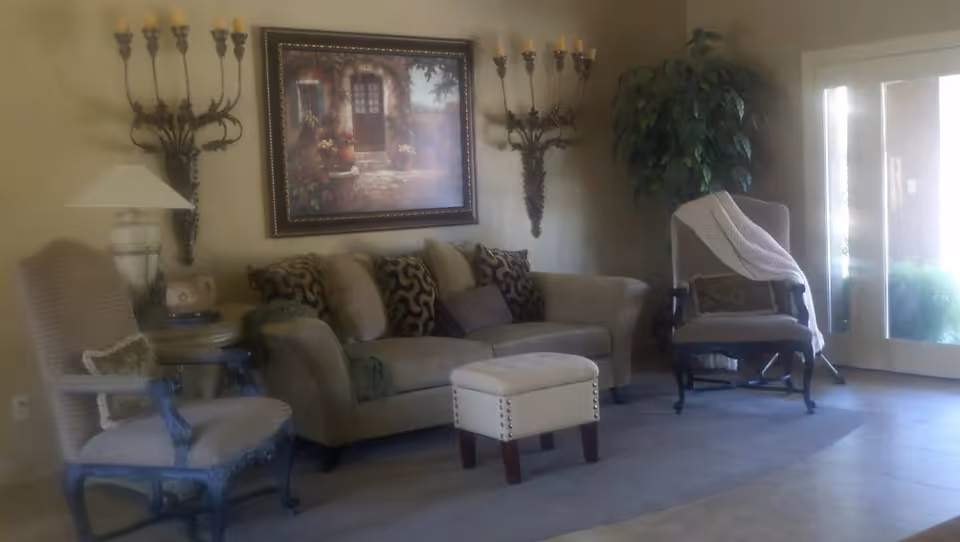 A cozy living room with a sofa, two armchairs, a small ottoman, decorative wall art and candle sconces beside a glass patio door.