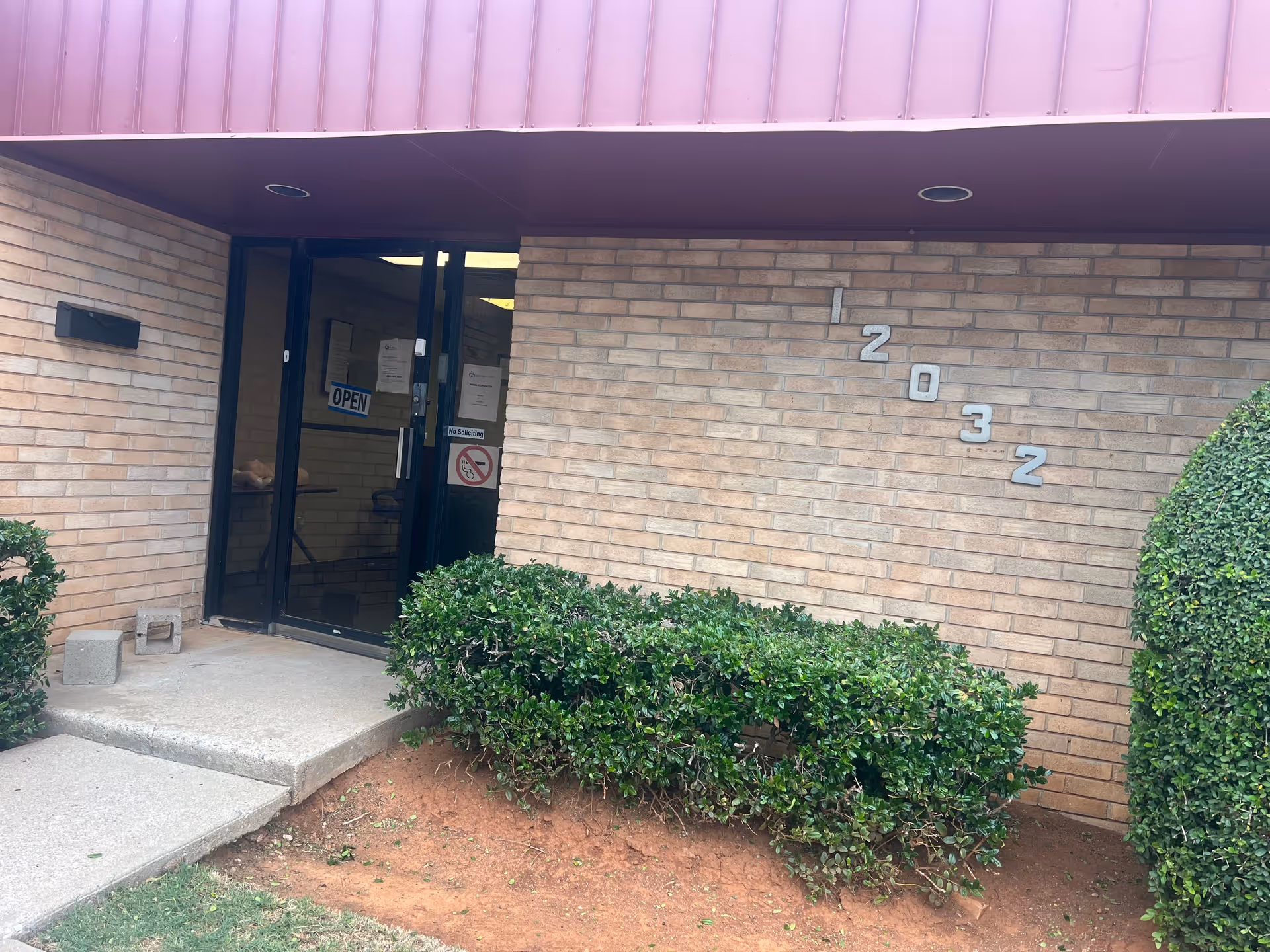 Entrance of Glory Healthcare LLC, brick building with glass doors and surrounding hedges.