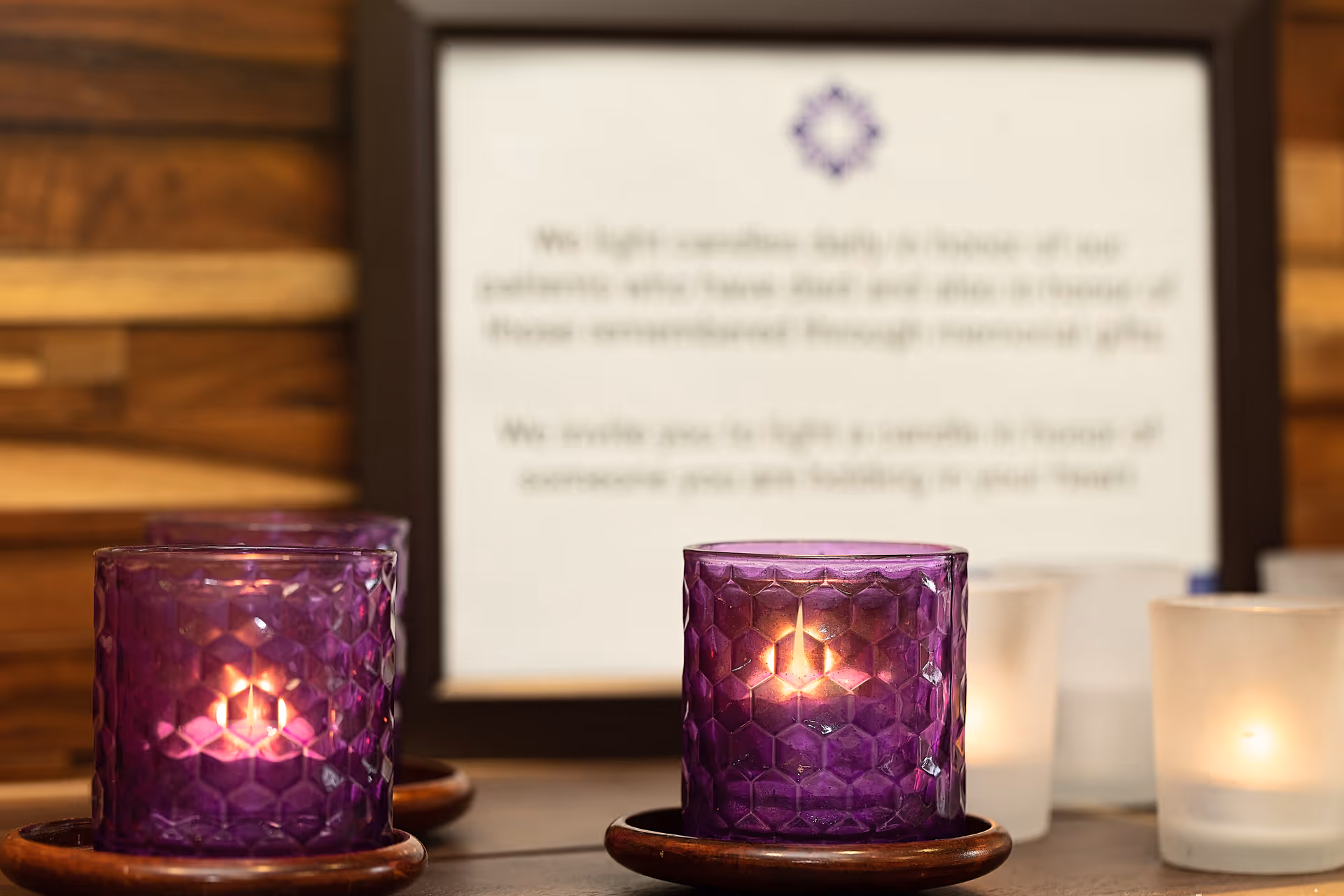 Dim purple candles on a table with a framed sign blurred in the background.