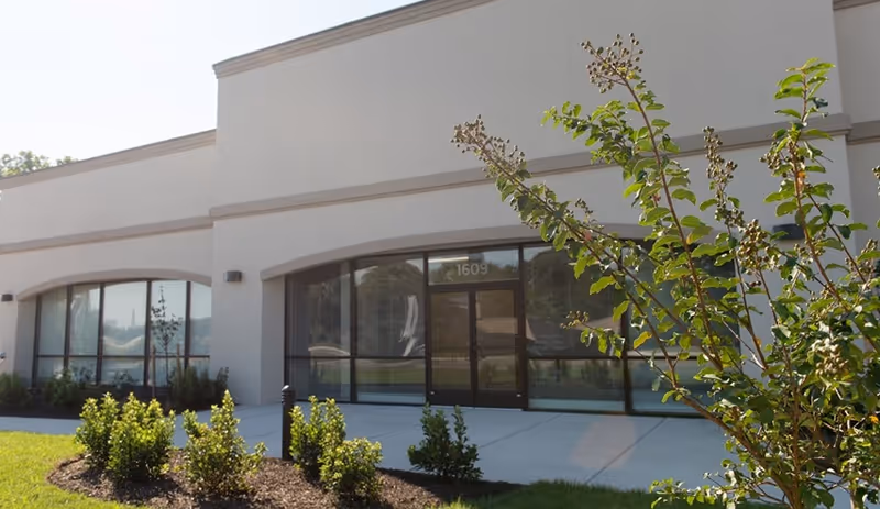 Exterior view of a building entrance with glass doors and landscaping.