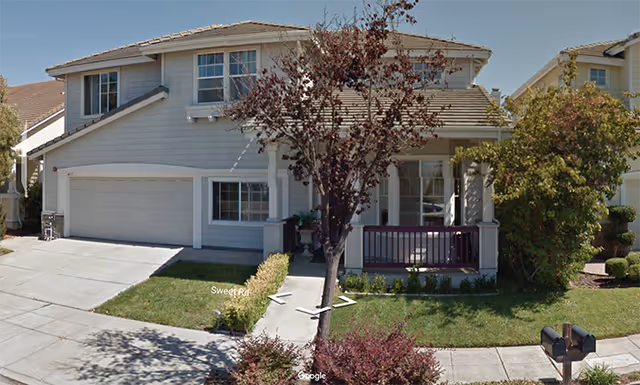 Two-story suburban house with attached garage, front porch, and trees.