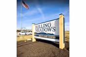 Outdoor sign reads Rolling Meadows Health Care Center beside a flagpole.