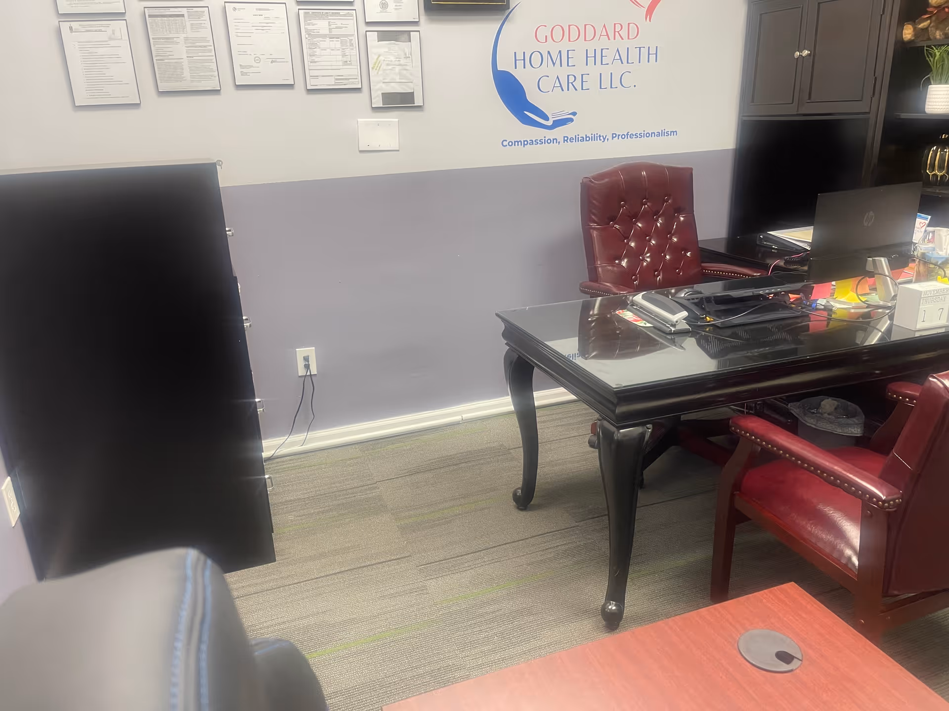 Reception area with glass desk, red leather chairs, and framed certificates.