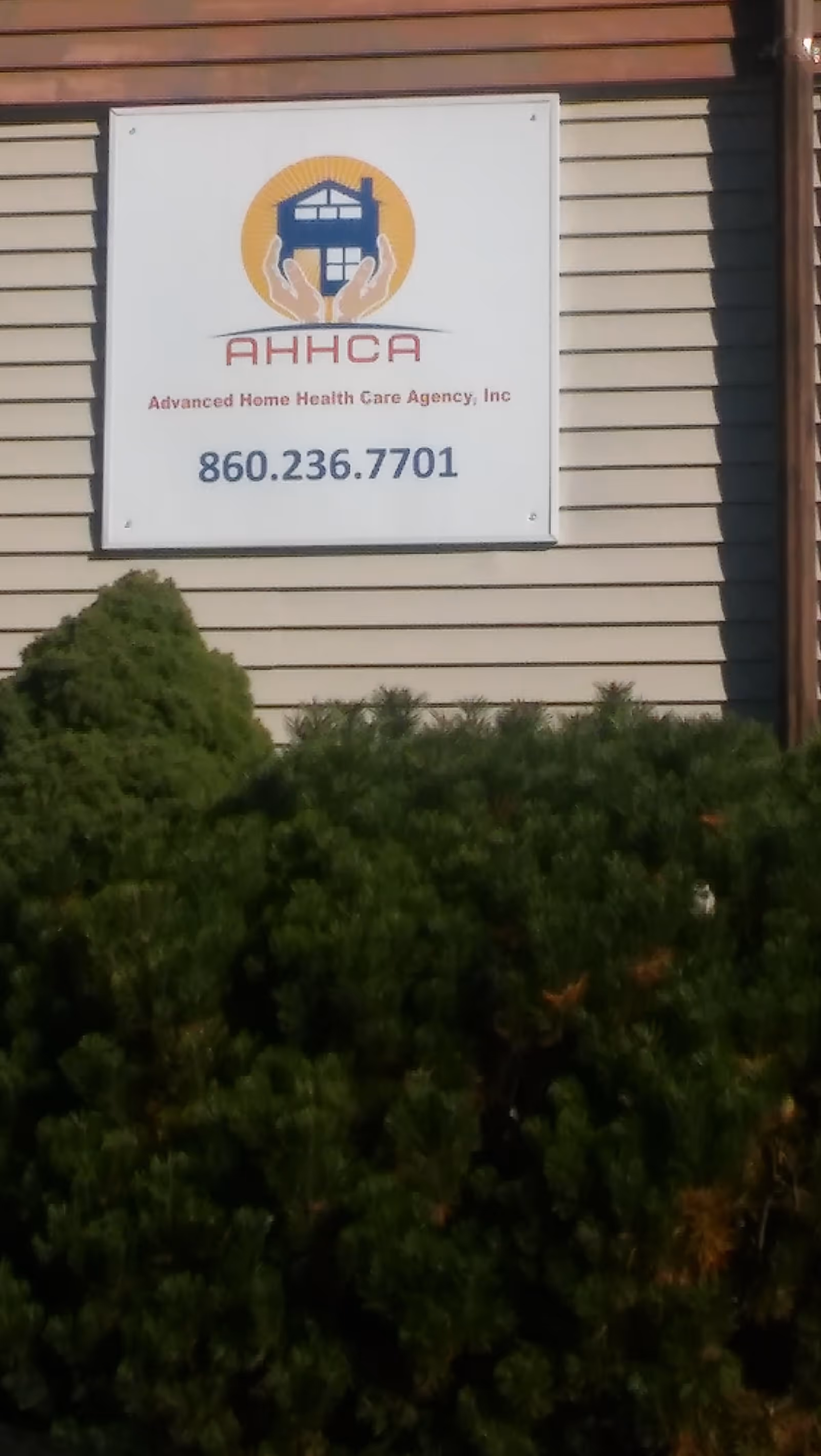 Exterior wall sign for Advanced Home Health Care Agency with logo, phone number, and shrubs.
