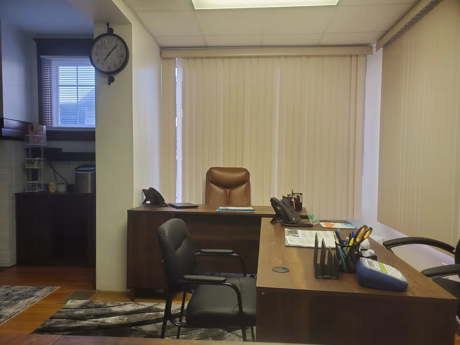 Office reception area with desk, chairs, blinds, and a wall clock.