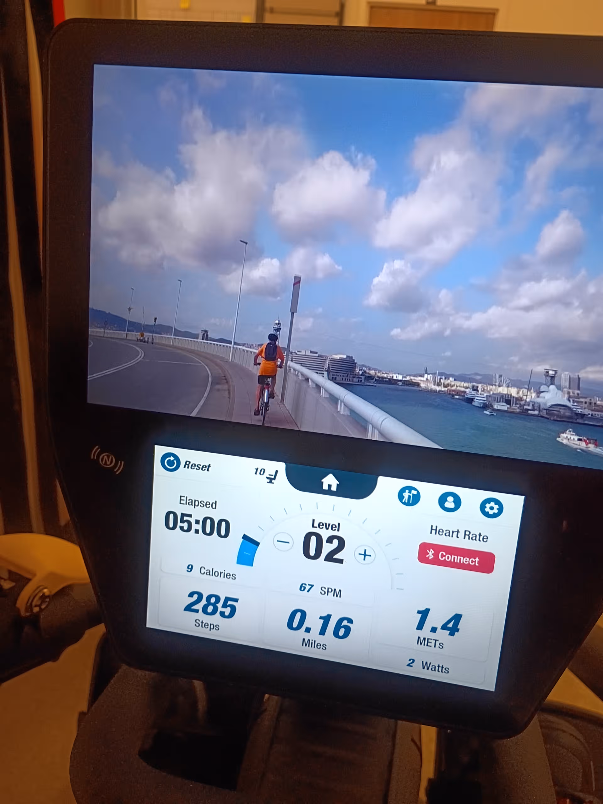 Close-up of a stationary bike console displaying a cyclist on a waterfront route.
