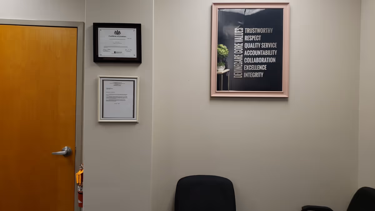 A neutral hallway features a wooden door, framed certificates, a motivational poster, and a black chair.