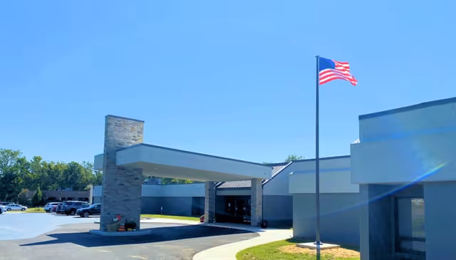 Exterior view of a modern hospital entrance with a covered drop-off and flagpole.