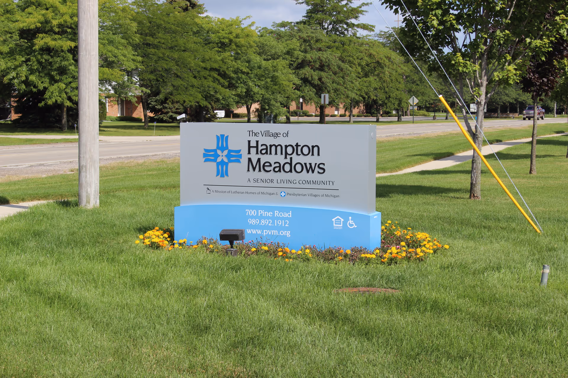 Outdoor sign for The Village of Hampton Meadows on a grassy, tree-lined lawn