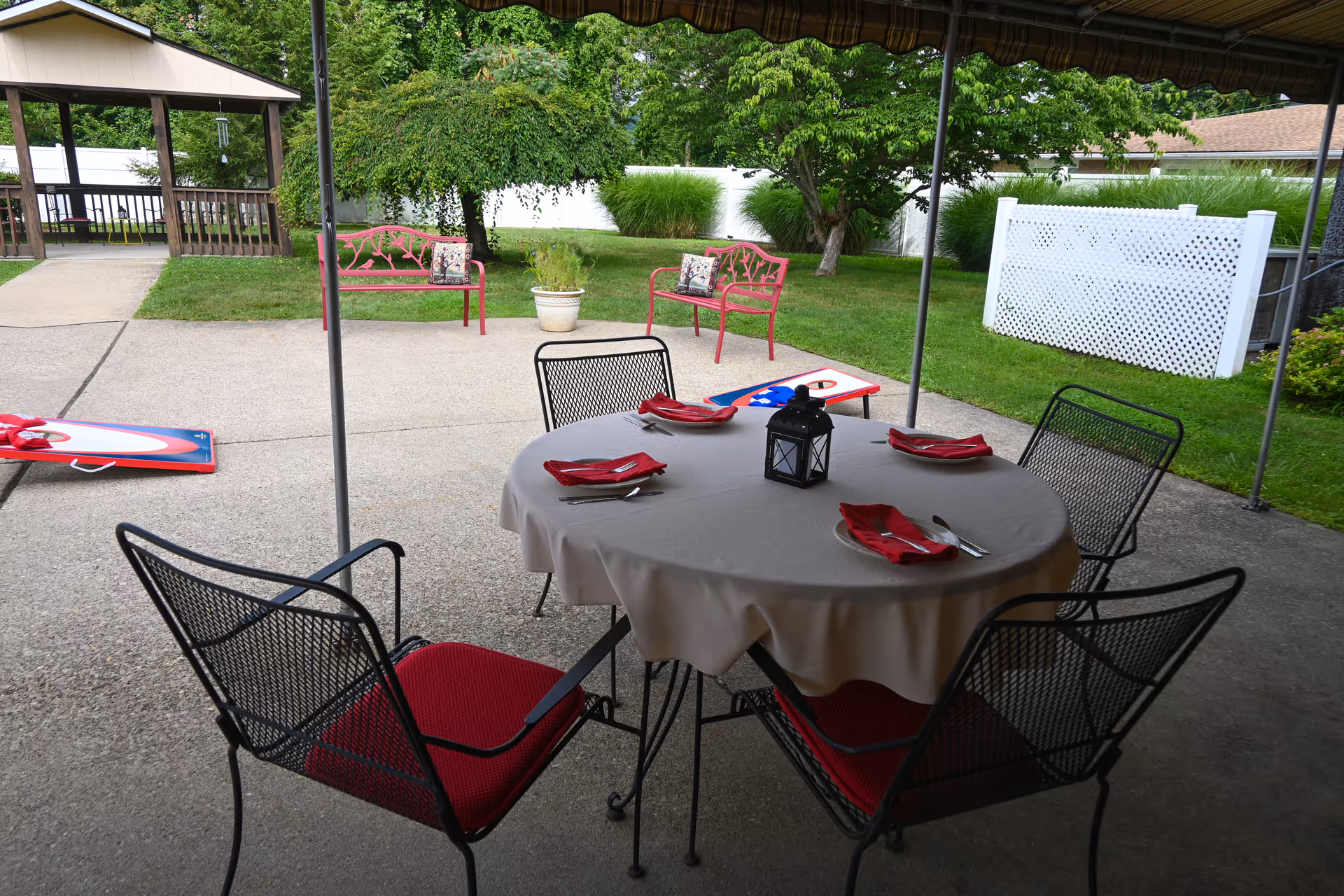 Outdoor covered patio with a round dining table, napkins, and a lantern centerpiece.