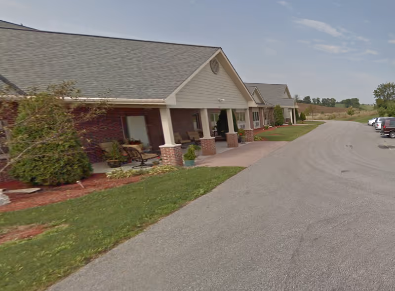 Single-story brick senior living buildings with porches line a curved driveway.