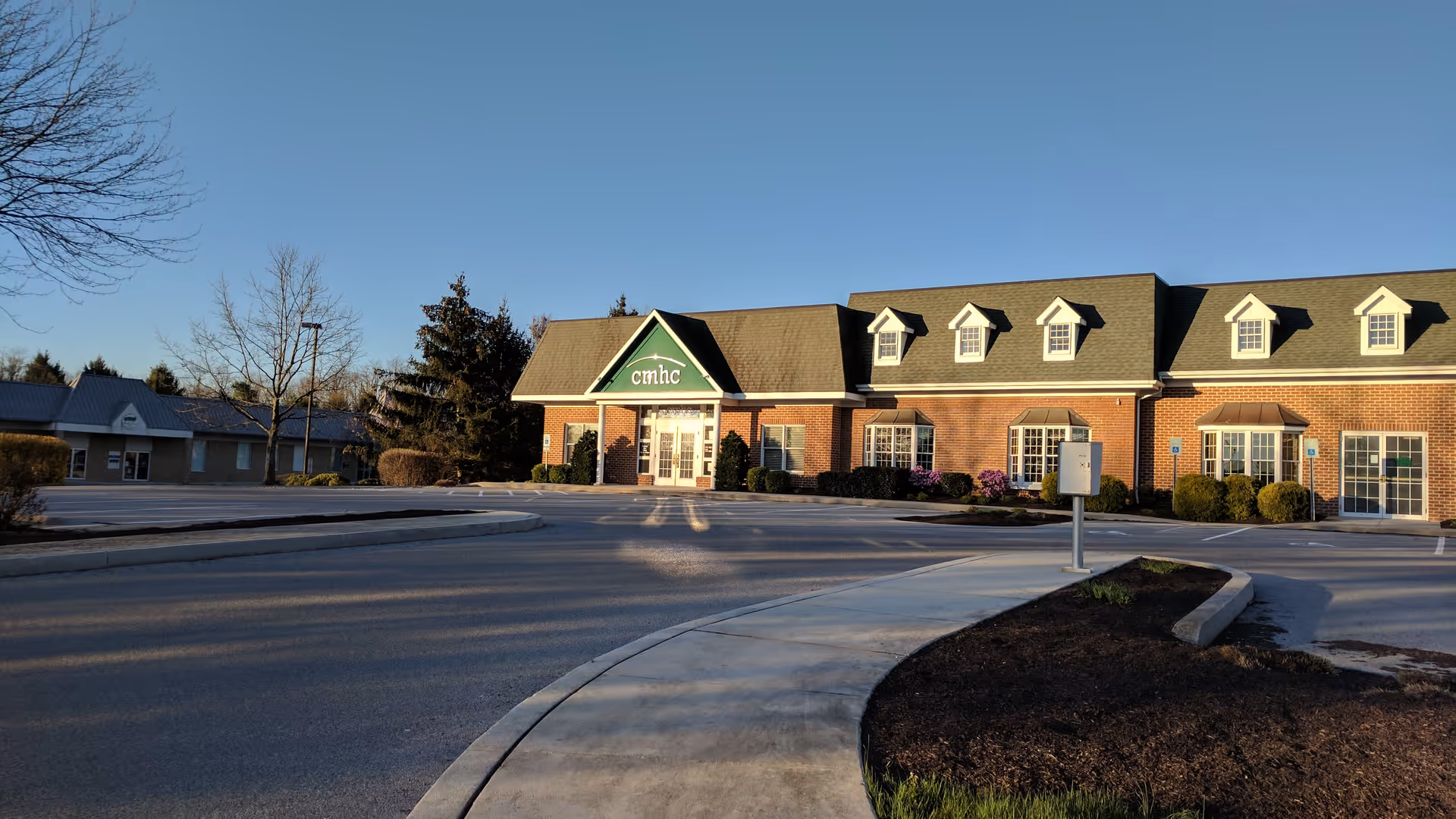 Exterior view of a brick senior living facility with a green entrance awning and parking.