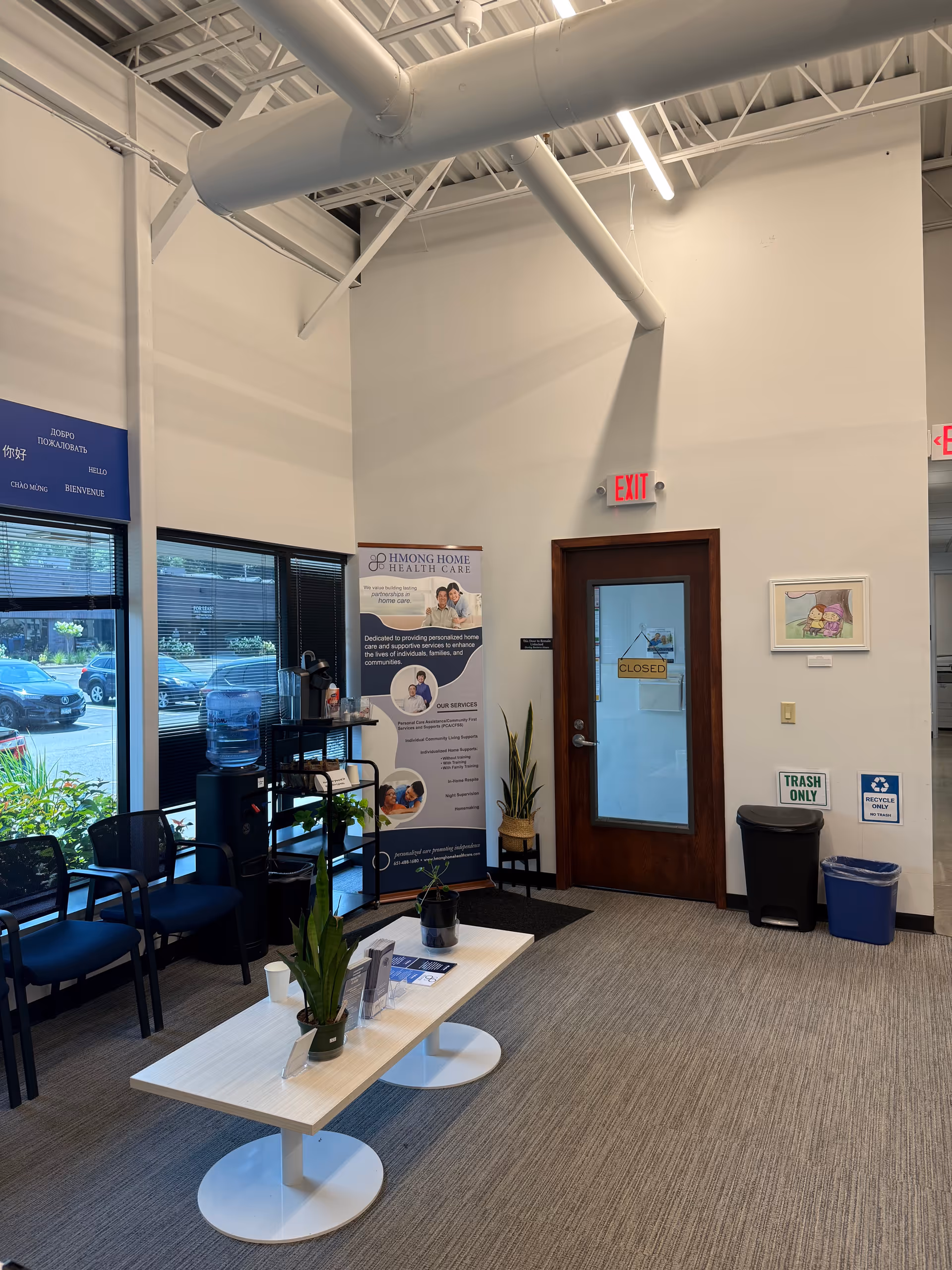 Interior reception area with seating, plants, a banner, water cooler, and a closed door.