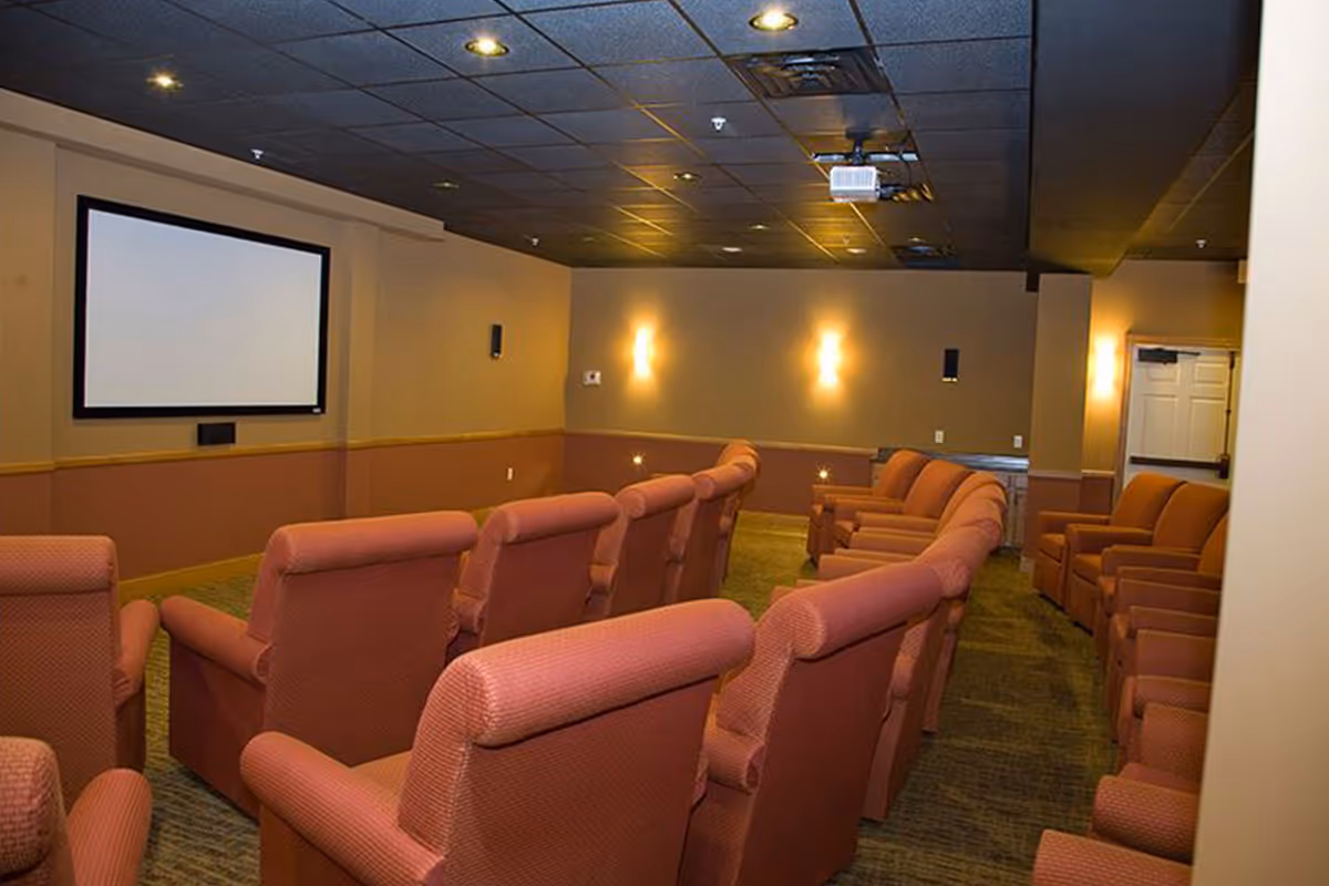 Private screening room with rows of pink upholstered recliner seats facing a large projection screen and ceiling-mounted projector.