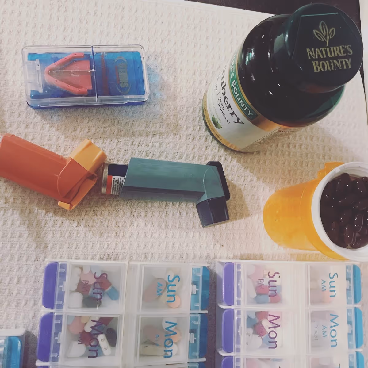 Close-up of pill organizers, vitamins, and bottle on a textured table.