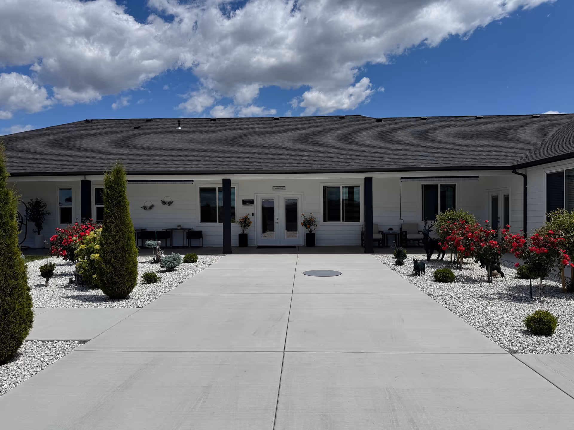 Single-story white facility exterior with central entrance, landscaped gravel beds, and flowering shrubs.