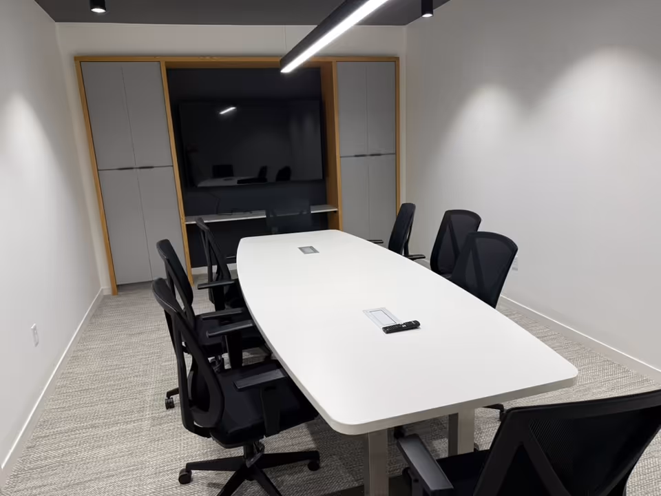 Modern interior conference room with white oval table, black chairs, and wall-mounted screen.