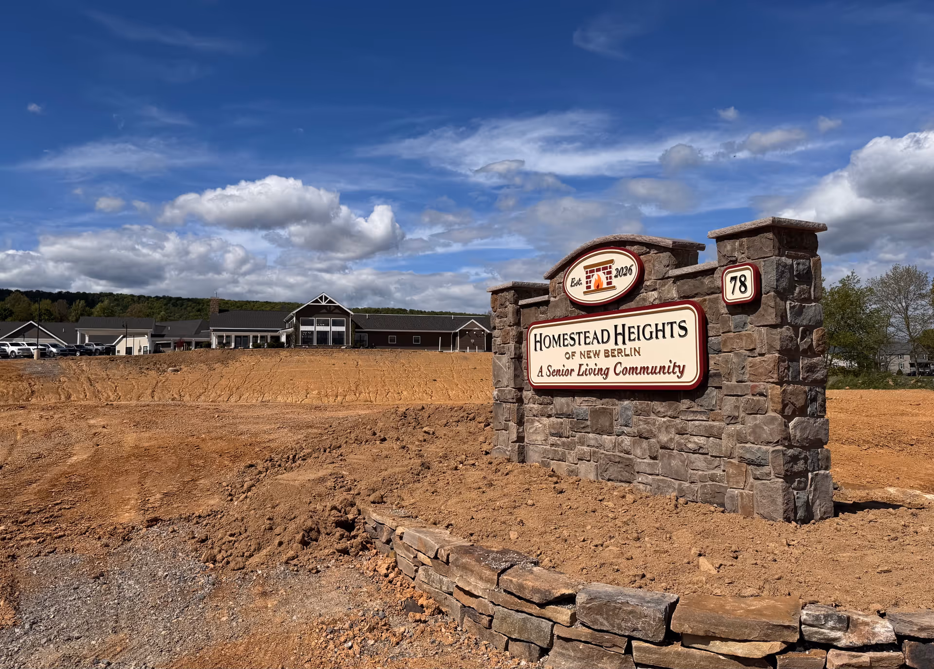 Stone entrance sign reads Homestead Heights of New Berlin with a building under construction behind