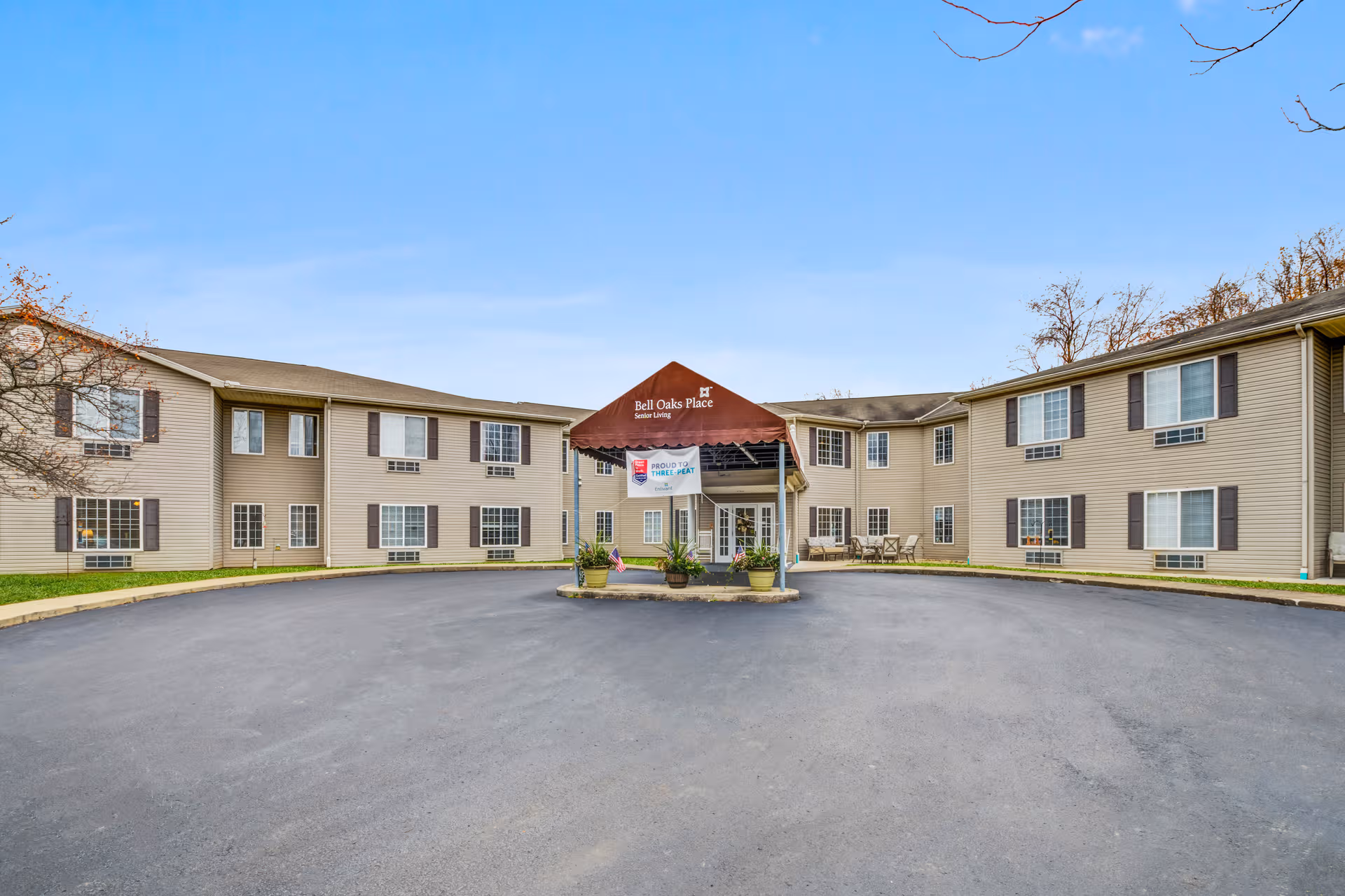 Two-story beige senior living building with a central entrance canopy and circular driveway.