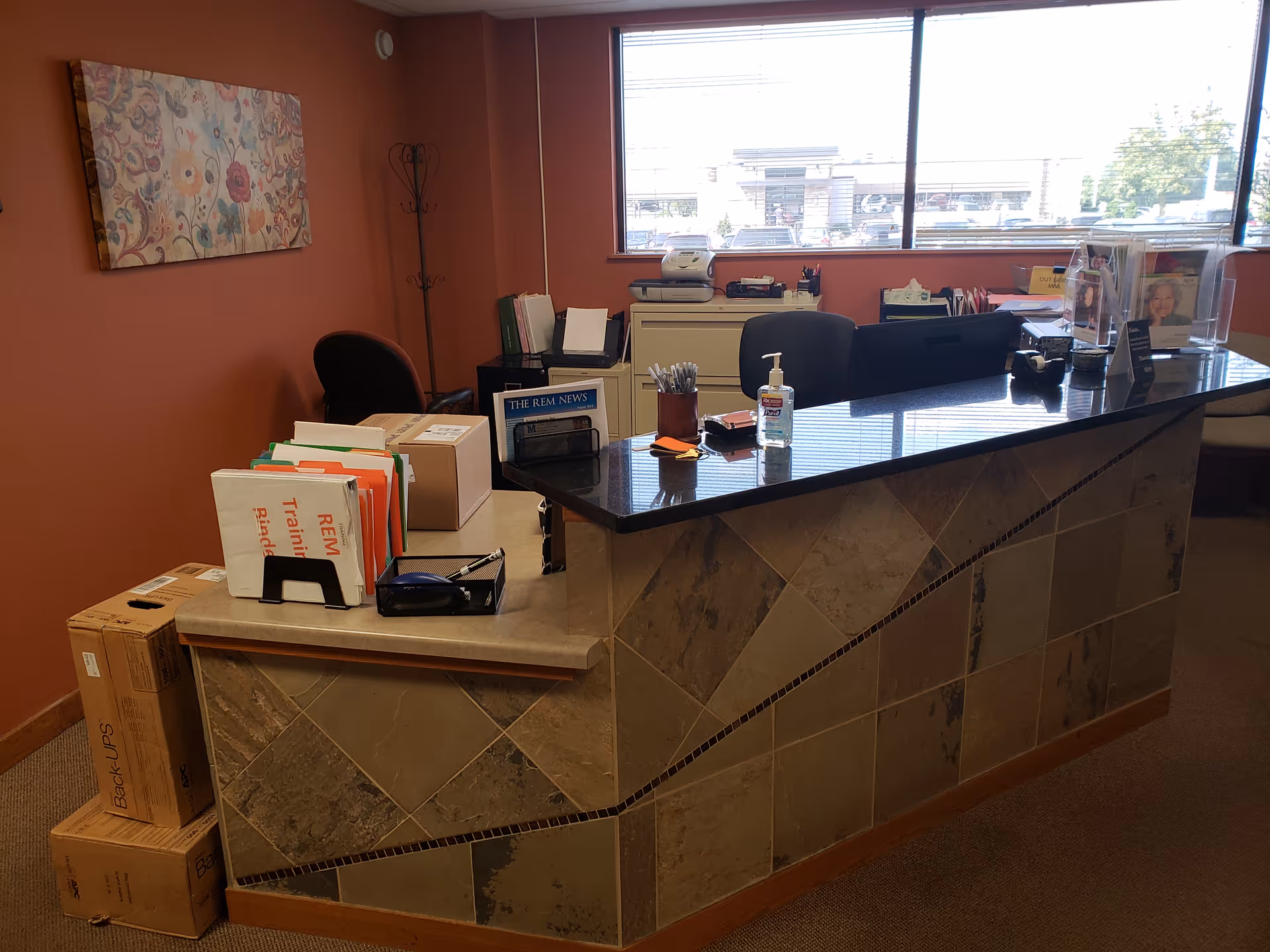 Reception desk with files, sanitizer, and office equipment in a warm senior living lobby.