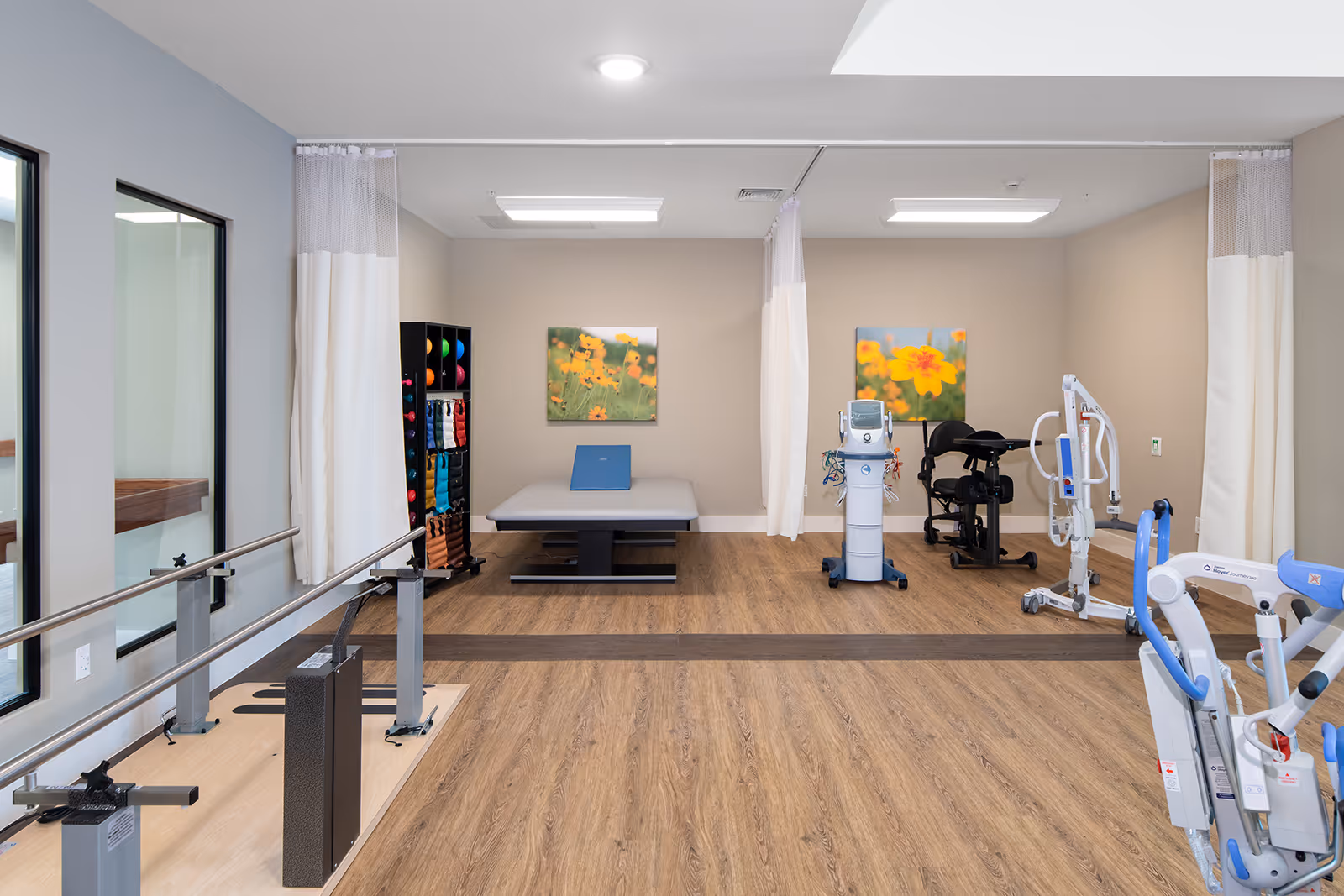 Indoor rehabilitation gym with exercise machines, a therapy table, and curtains.